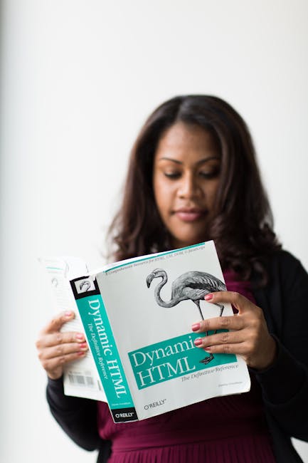 The image shows a woman with long, dark brown hair examining a book titled 'Dynamic HTML' by O'Reilly, which features a detailed illustration of a flamingo on the cover. She is dressed in a black blaz